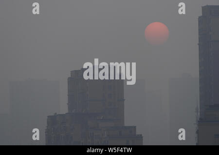 The sun and high-rise buildings are seen vaguely in heavy smog in Dalian city, northeast China's Liaoning province, 4 March 2019. Stock Photo