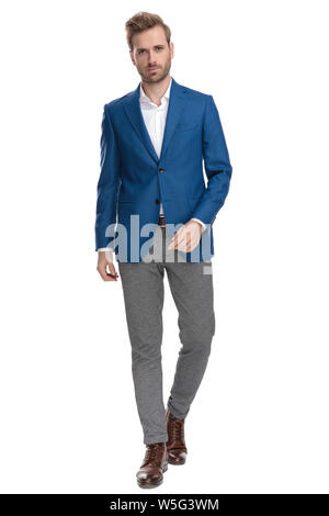 Serious looking casual man confidently walking forward while wearing an elegant suit on white studio background Stock Photo
