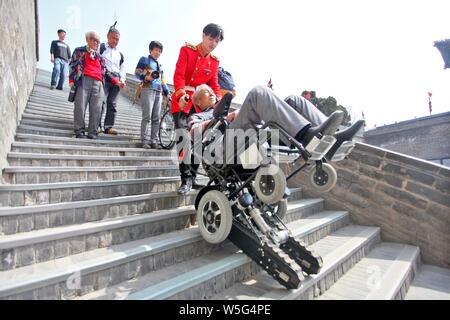 A Chinese attendant helps an 84-year-old tourist downstairs on a stair-climber wheelchair from the ancient  city wall in Xi'an city, northwest China's Stock Photo