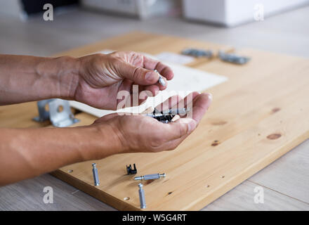 Man assembling furniture at home, male hand with wooden dowel pins and screws. Stock Photo