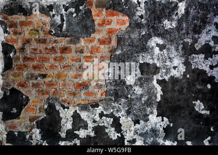 Wall with a burnt peeling paint, now black used to be white, revealing brick structure under plaster in an old, abandoned building, grunge background