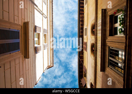 View up at vibrant blue sky with white clouds between two old houses in the city center of the capital of Italy, Rome on a warm fall morning. calm atm Stock Photo