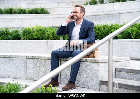 Mature Businessman Taking Phone Call On Mobile Sitting At Outside Office Building Stock Photo