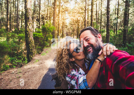 Cheerful people beautiful adult cacuasian couple enjoying outdoor leisure activity traveling in the forest and kissing each other with fun and happine Stock Photo