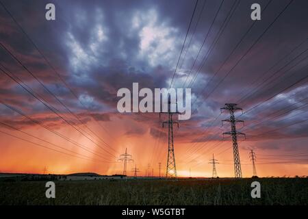 Extreme weather. Electricity pylons with power lines against stunning storm at sunset. Stock Photo