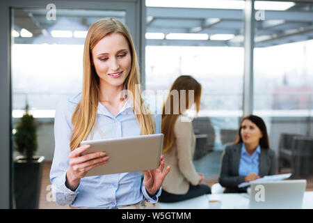 Pretty secretary holding a digital tablet and looking at it Stock Photo
