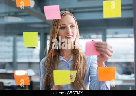 Business plan. Young female professional sticking colourful notes to a glass wall Stock Photo