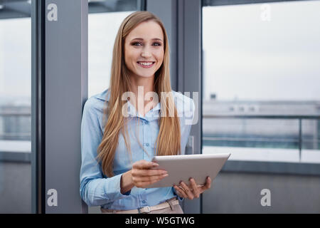 Cheerful woman at office standing with digital tablet Stock Photo