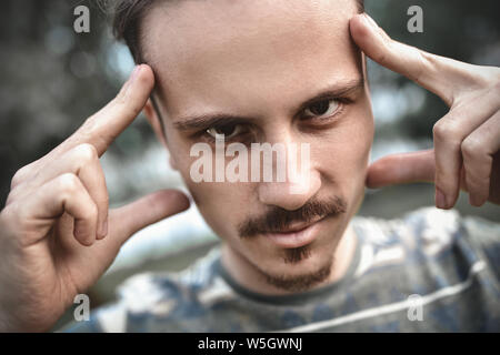 mind games and brain power. mentalist and cognitive skills concept. man concentrating and holding index fingers on temples. young bearded guy portrait Stock Photo