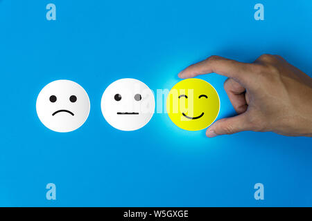 Conceptual the customer responded to the survey. The client using hand choose happy face smile icon on blue background.Depicts that customer is very s Stock Photo