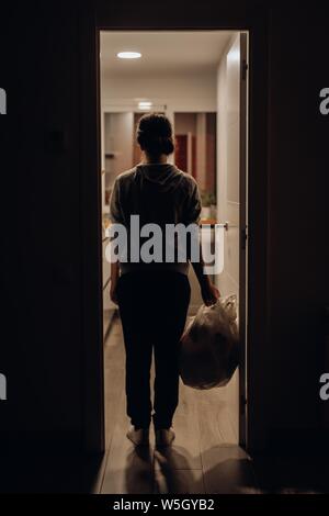 Vertical shot of a female holding plastic bag filled with groceries and standing at the door jamb Stock Photo