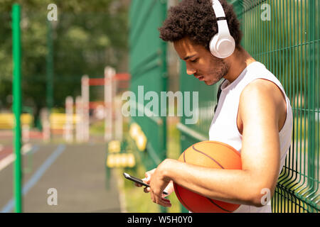 Young contemporary basketball player in headphones scrolling in smartphone Stock Photo