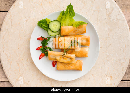 Tasty looking spring rolls served on a round plate with garnish - food concept flat lay image with copy space for text. Stock Photo