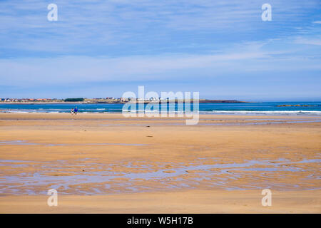 View across a quiet sandy beach and bay on northeast coast to village of Beadnell, Northumberland, England, UK, Britain Stock Photo