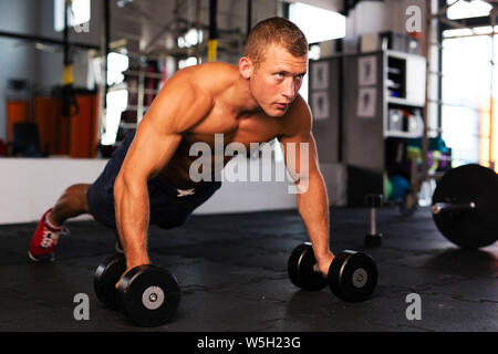 Young man doing pushups on dumbbells at gym Stock Photo