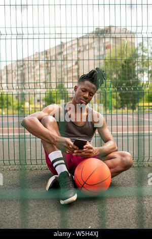 Restful African guy in sportswear scrolling or texting in smartphone Stock Photo