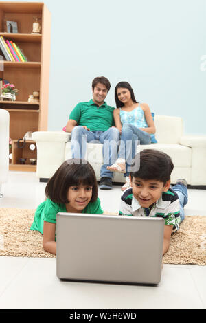 Boy and girl using laptop with their parents sitting on couch Stock Photo