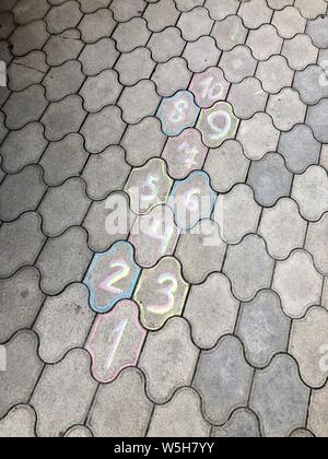 Drawings on the asphalt for children's play. Hopscotch court with numbers from 1 to 10 drawn with white chalk on the asphalt.Child playing hopscotch g Stock Photo