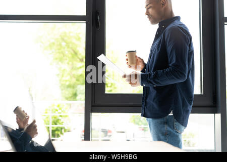 Successful African entrepreneur studying documents with attentive and concentrated look, drinking coffee Stock Photo