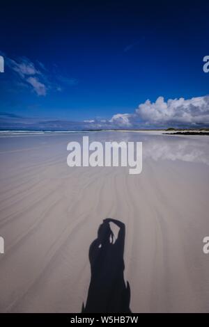 Vertical shot of a clear water seashore and a male shadow over sand with dark blue sky Stock Photo