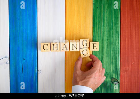 Male hand changing the word Change in to Chance by switching letters G and C over a colourful wooden background. Stock Photo