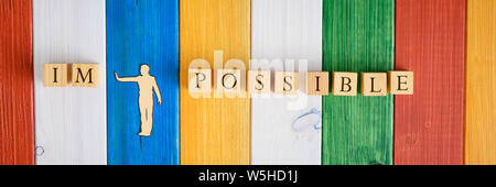 Paper cut silhouette of a man pushing away letters Im from the word Impossible made of wooden blocks. Over colourful background of wooden planks. Stock Photo