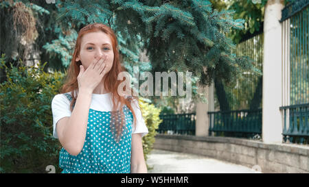 Smiling beautiful redhead woman covered mouth with laughter. Freckled ginger girl laughs at joke with copy space. Cute funny red-haired teenager stand Stock Photo