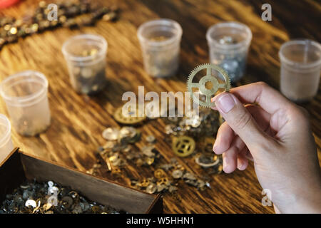 Watchmaker holds large gear. Cogwheel on blurred background of workplace. Pinion in female hand. Old cogwheel on wooden table background. Big metal ge Stock Photo