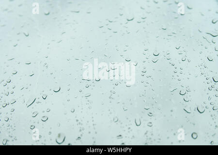 Rain drops on grey background  on rainy day on outside window glass. Beautiful view of grey sky backdrop. Water drops on glass with blurred edges. Stock Photo