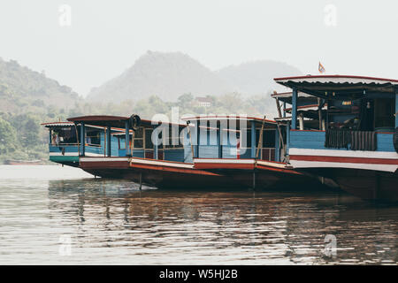 Traditional Laotian wooden slow boats on Mekong river near Luang Prabang at sunset, Laos. Mountain on background Stock Photo