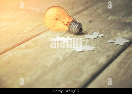 bulb and connected white puzzle pieces on table Stock Photo