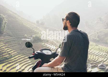 Bearded young Caucasian man on red motorcycle overlooking rice terraces of Sapa in Lao Cai region, Vietnam Stock Photo