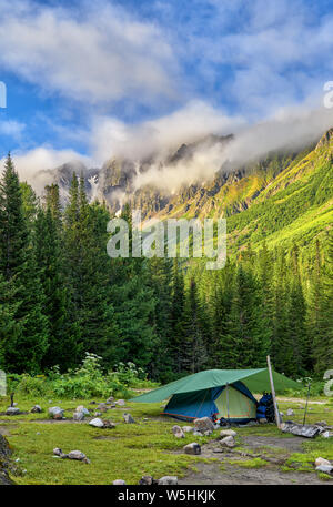Tent backpackers installed on edge of dark forest. Siberian summer morning in mountains. Eastern Sayan. Tuva Stock Photo