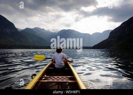 child in the front of a canoe paddling on the calm Bohinj lake, Slovenia, Europe Stock Photo