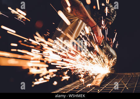 Worker Using Angle Grinder in Factory and throwing sparks. Stock Photo