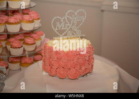 Pink cupcakes with large pink wedding cake, all set up on the wedding day waiting for the bride and groom to cut them at their wedding celebration Stock Photo