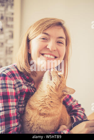 Red tabby cat is kissing a young beautiful girl, closeup Stock Photo