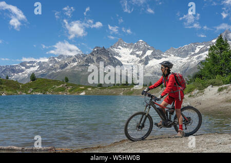 active senior woman, riding her electric mountainbikeon the Gornergrat in Zermatt, Wallis,Switzerland. In The background Weisshorn, Zinalrothorn and O Stock Photo