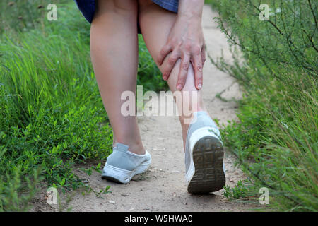 Ankle sprain, woman grabbed her leg while walking on a summer nature. Concept of pain in tired legs, injury on running Stock Photo