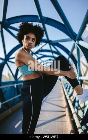 Woman athlete doing fitness workout on a walkway bridge in morning. fitness woman doing stretching workout of the legs. Stock Photo
