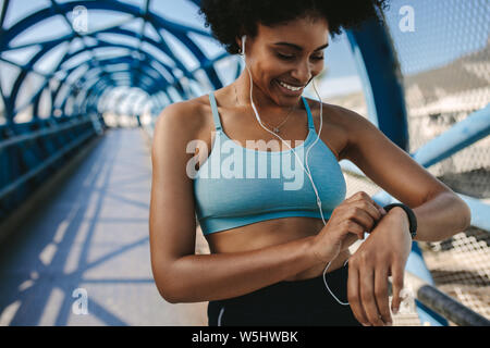 Fit female runner using smart watch to monitor her performance. African Woman setting fitness app on her smart watch before running session. Stock Photo