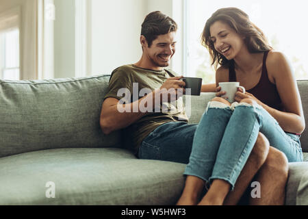 Happy young couple relaxing on couch at home with coffee. Young man and woman relaxing on sofa drinking coffee Stock Photo