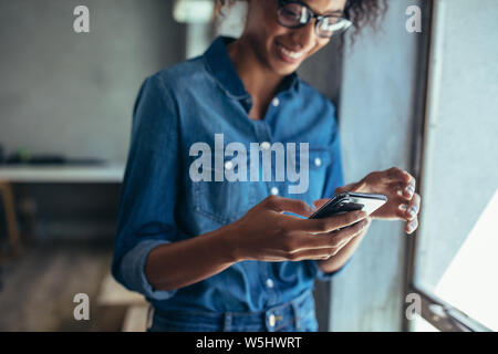 Female entrepreneur standing in office and using smart phone. Focus on mobile phone in hand of a woman wearing casuals. Stock Photo