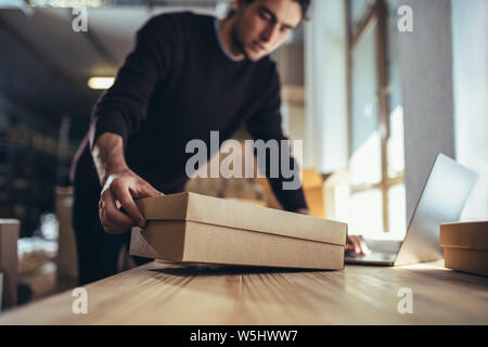 Small business owner with the box for shipping working on laptop. Male entrepreneur working on online orders. Stock Photo