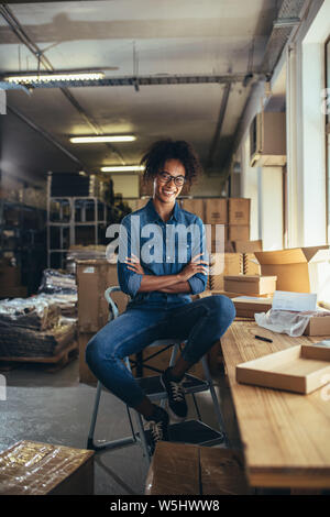 Smiling woman sitting at the desk with parcel boxes around. Female entrepreneur of a online selling store. Stock Photo