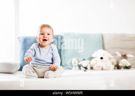 Adorable laughing baby boy sitting on sofa and looking up. Stock Photo