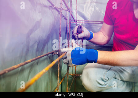 Closeup of a man hands wire with pliers metal rods constructing basement framework for concrete pouring Stock Photo