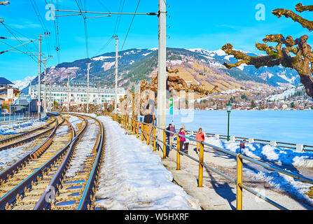 ZELL AM SEE, AUSTRIA - FEBRUARY 28, 2019: The cityscape with railroad, winter Elisabeth park, frozen Zeller See lake and luxury Grand Hotel on backgro Stock Photo