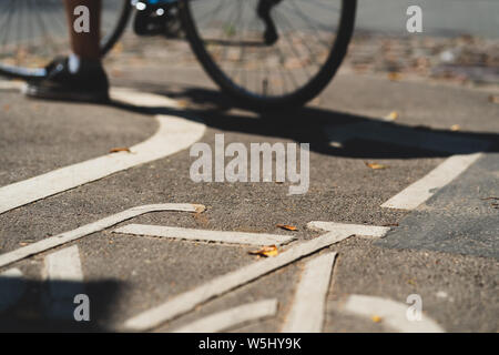 A cyclist stands on a bike path with a bicycle stencil on gray asphalt with yellow leaves in summer