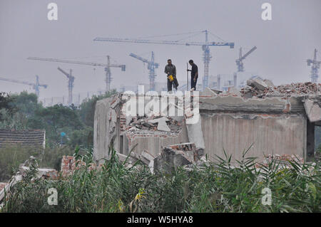 Two workers demolish a building as tower cranes build new housing in the background Stock Photo